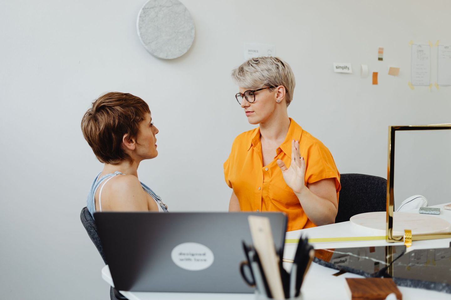 Zwei Mitarbeiterinnen besprechen an einem hellen Arbeitsplatz eine Frage am Notebook.