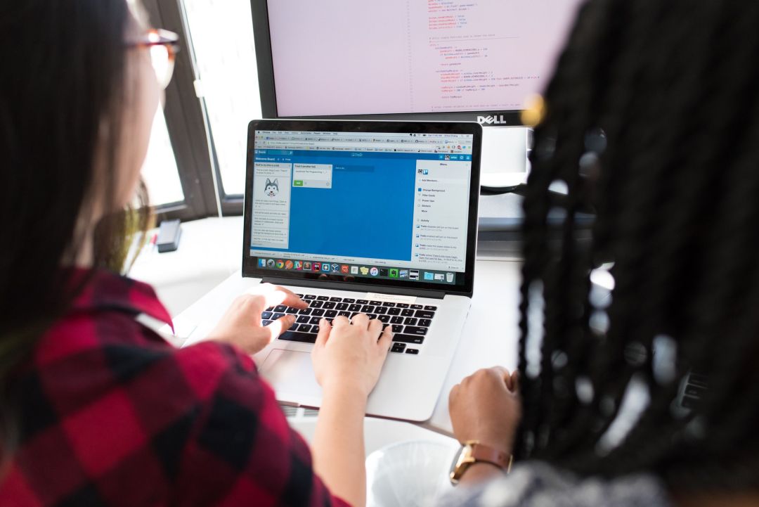 Zwei Personen arbeiten gemeinsam an einem Notebook vor einem großen Monitor.
